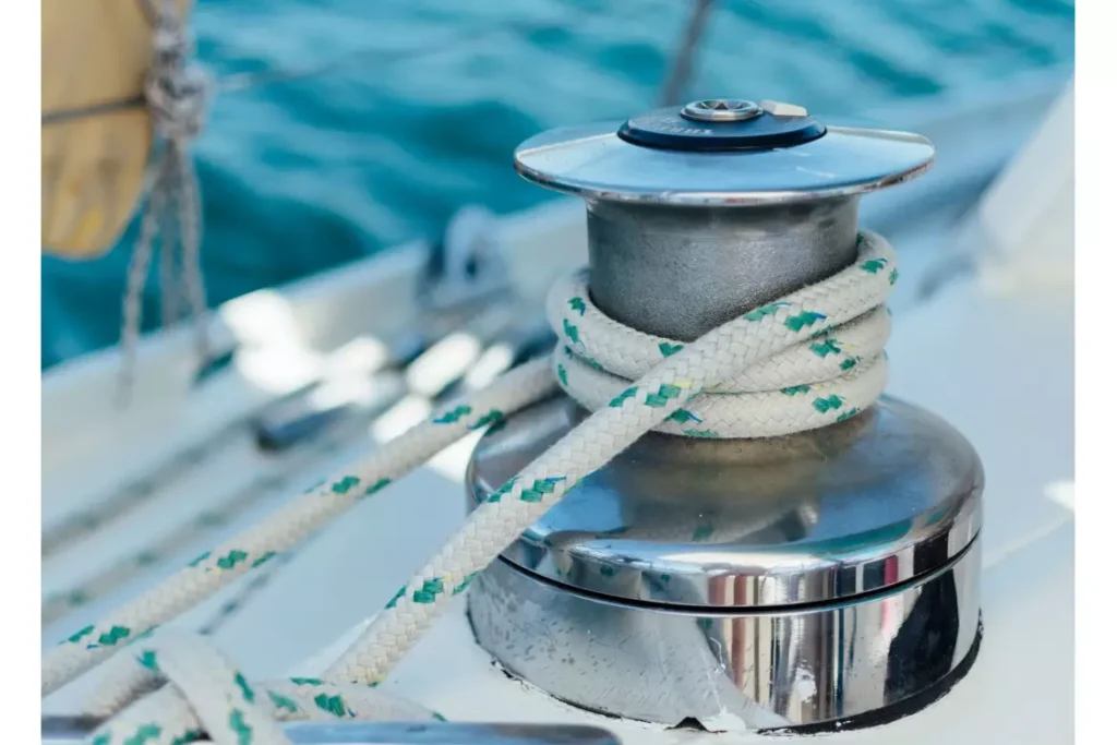 Winch chromé avec corde marine blanche et verte sur un voilier en navigation, arrière-plan de mer bleue.