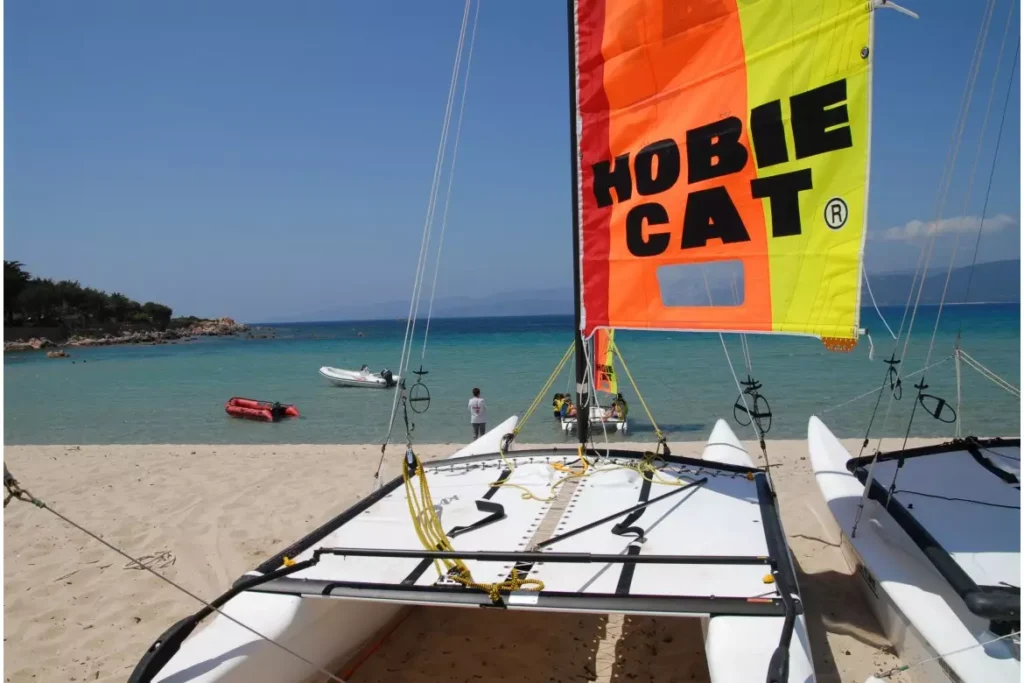 Catamaran Hobie Cat à voile orange et jaune sur une plage de sable blanc bordant une eau turquoise.