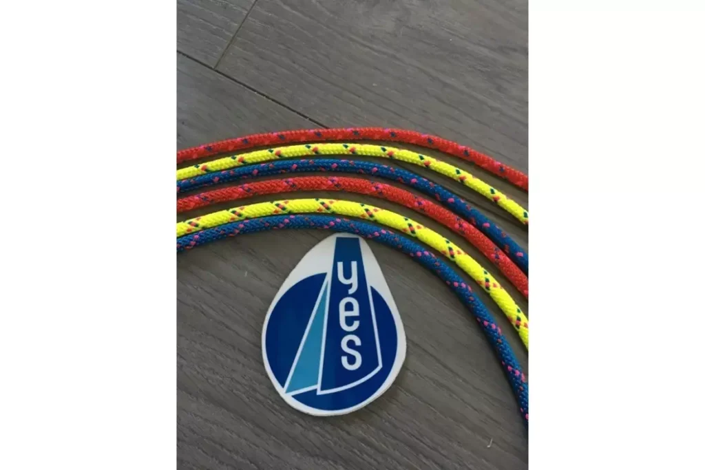 Cordages nautiques rouge, jaune et bleu avec autocollant YES et logo voile sur un sol gris.