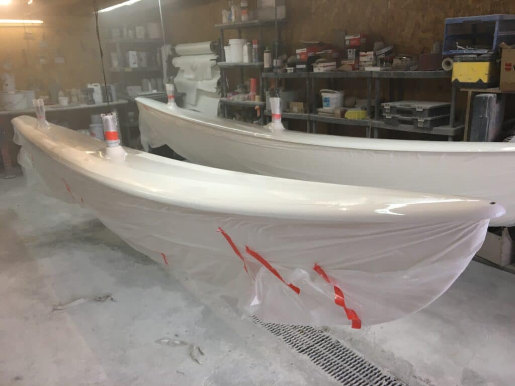 Atelier de fabrication et réparation de coques de bateaux Coques de bateau blanches suspendues dans un atelier en cours de finition, protégées par des bâches et du ruban adhésif.