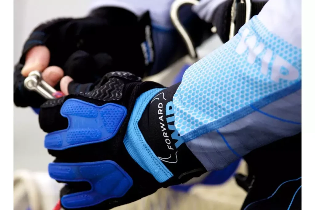 Gants de voile Forward WIP manipulant une manille. Équipement nautique technique haute performance noir et bleu.